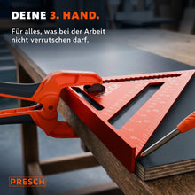 Federzwinge hält einen Anschlagwinkel auf einer Arbeitsplatte fest, während eine Schraube eingedreht wird.