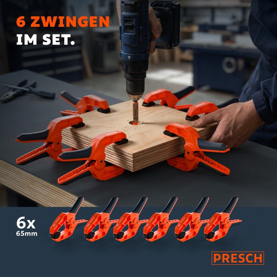 Sechs Federzwingen umschließen sternförmig ein Holzbrett, in dessen Mitte gerade gebohrt wird.