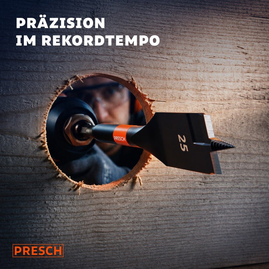 25mm Flachfräsbohrer schaut durch ein frisch gebohrtes Loch in einem dunklen Holzbrett, Handwerker mit Schutzbrille blickt hindurch