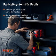 Een monteur reikt in het magazijnrek naar een doos zwarte handschoenen; het kleurensysteem op de verpakking maakt een snelle maatbepaling mogelijk.