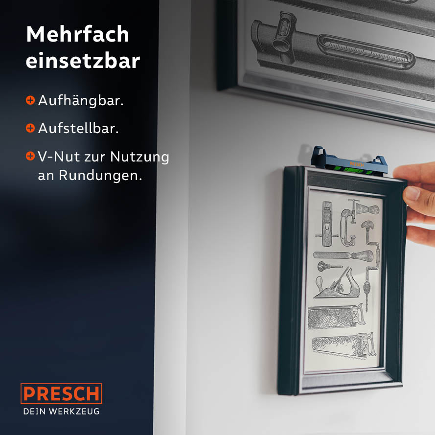 Die kleine, orangefarbene Wasserwaage ist an einer blauen Schnur eingehängt, die über einem hellen Holz balken gespannt ist. Die Libelle zeigt eine waagerechte Ausrichtung an. Im Hintergrund ist ein angedeuteter Werkstattbereich zu erkennen.