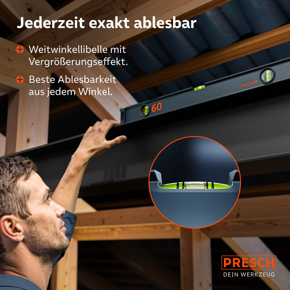 Die magnetische 60cm Wasserwaage haftet an einem Stahlbalken bei der Deckenmontage; eine Lupengrafik zeigt die Weitwinkellibelle mit Vergrößerungseffekt für präzises Ablesen über Kopf.