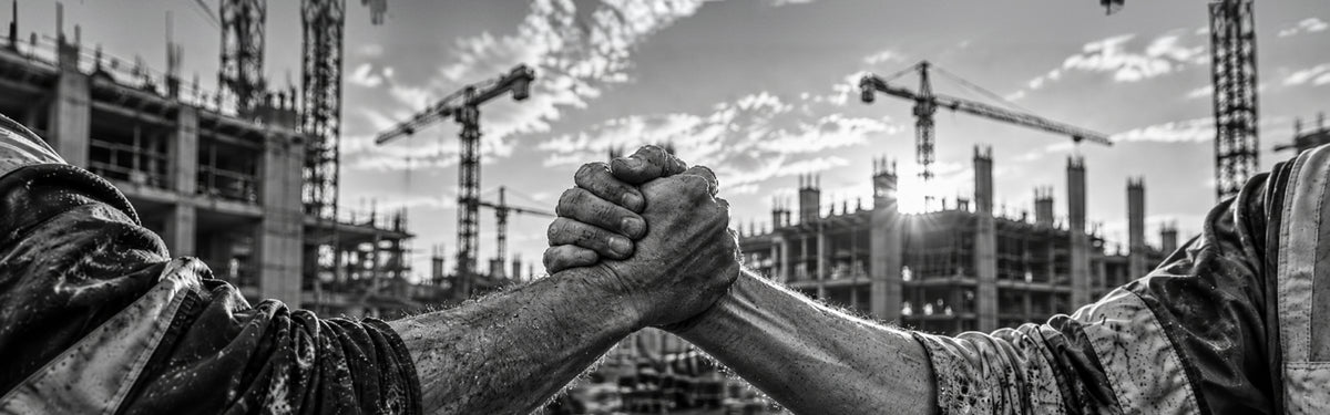 Zwei Handwerker reichen sich vor einer Baustelle mit Kränen die Hand